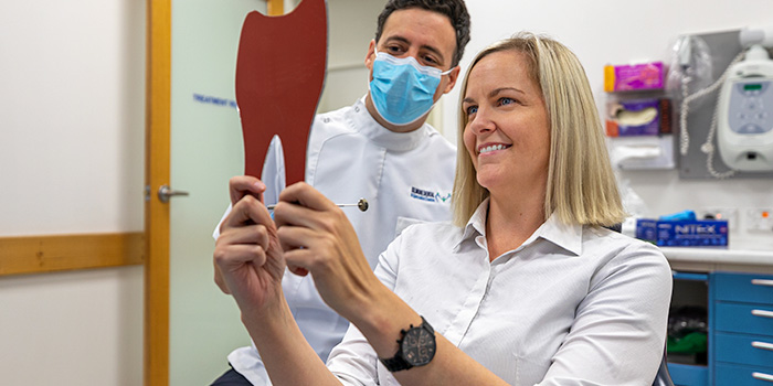 A patient is holding a tooth shaped mirror with a dentist looking over her shoulder