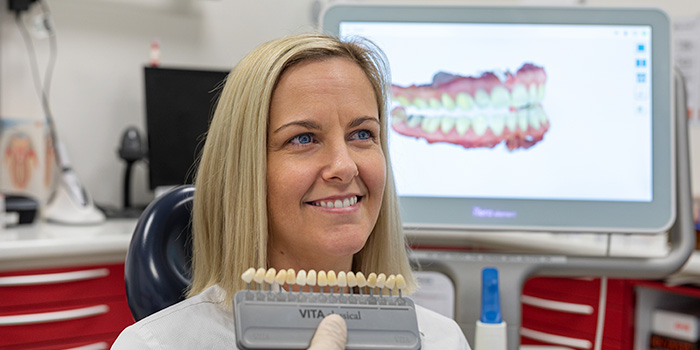 A dentist holding up a row of fake teeth intended to demonstrate with a diagram of the mouth in the background