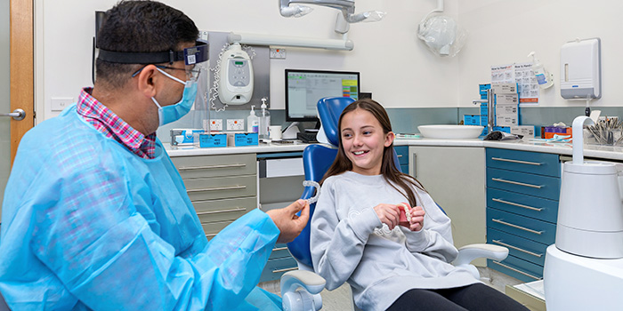 A dentist holds up a set of Invisalign to a young female patient who in a dental office.